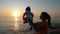 Mother holds baby in her arms while looking at sunset by the sea or ocean shore.