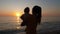 Mother holds baby in her arms while looking at sunset by the sea or ocean shore.