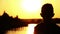 Mother hugging her son near the river at sunset silhouetted dawn, glare on water