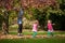 Mother and identical twins having fun with autumn leaves in the park, blond cute curly girls, happy kids, girls in pink jacket