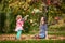 Mother and identical twins having fun with autumn leaves in the park, blond cute curly girls, happy kids, girls in pink jacket