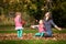 Mother and identical twins having fun with autumn leaves in the park, blond cute curly girls, happy kids, girls in pink jacket