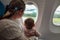 Mother and infant baby in the airplane near the window. The look at the ground and enjoy the flight. Travel with children under