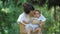 Mother kisses her Baby holding the child in hands on a green background of grass and trees. Happy young Mother holds her