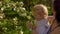 Mother and a little blonde daughter are sniffing flowers on the apple tree