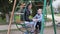 Mother and little curious son sitting together on swing in park