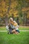 Mother and little daughter blonde with Teddy bear seating on green grass in autumn park