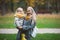 Mother and little daughter blonde with Teddy bear seating on green grass in autumn park, close up