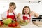 Mother and little daughter cooking together with cook apron preparing salad at home kitchen