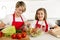 Mother and little daughter cooking together with cook apron preparing salad at home kitchen