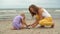 Mother with little daughter playing with pebble stones on the beach