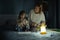 Mother and little daughter studying and drawing in a complete darkness during electricity outage. Little girl uses camping lantern