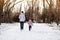 Mother and little girl in colored jackets jogging by snow in winter park. Concept of instill sports health habits