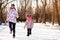 Mother and little girl in colored jackets jogging by snow in winter park. Concept of instill sports health habits