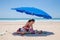 Mother and little girl down blue parasol at beach