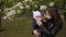 A mother in a medical mask holds a child in a Park near blooming tree.