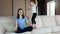 Mother meditating sitting on sofa while active child daughter jumping playing
