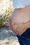Mother pregnant woman embracing her naked abdomen belly with caress hands outdoor