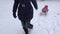Mother pull daughter baby on sledge along snow in winter resort. Handheld. 4K