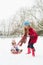 Mother Pulling Daughter On Sledge Through Snow