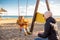 Mother pushing her infant baby boy child on a swing on sandy beach playground outdoors on nice sunny cold winter day in