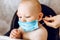 Mother puts a medical protective mask on the face of her young child, the Child is sitting in a feeding chair. Quarantine,