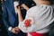 Mother putting on stylish groom in blue suit boutonniere with pink roses in hotel room. Morning preparation before wedding