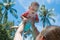 Mother raised up infant child high above the head in the pool. The little baby girl is very happy and screams for joy. Summer