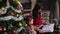 Mother reads a book for her daughter near the Christmas tree.