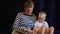 Mother reads a book to a baby sitting on a mattress