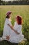 mother with red hair and a hat is sitting in a green field with grass with her daughter of four years sunset