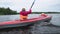 Mother rows bright orange sport kayak with little kid sailing along lake against forest and cloudy grey sky on nasty day