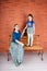 Mother sits on the bench and daughter stays in front of red brick wall.