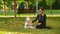 Mother sits with his lovely cute infant daughter on autumn lawn in pictorial city park with trees and fallen yellow leaves