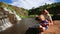 Mother Sits Holds on Knees Little Girl Makes Selfie by Waterfall