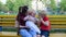 Mother sitting in  Park with baby and elder son. Brother entertains his sister