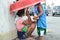 Mother sitting on pavement with siblings using umbrella cuddling baby son at church yard