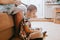 Mother sitting on the sofa braids her daughter`s hair sitting on the floor next to her in the cozy light room