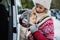 Mother with sleeping small daughter in carrier standing by car in winter nature.