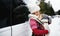 Mother with sleeping small daughter in carrier standing by car in winter nature.