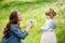 Mother with small daughter blowing to dandelion - lifestyle outdoors scene in park. Happy family concept