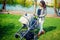 Mother smiling with baby in park. Mother walking child with pram or baby stroller