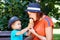 Mother and son in blue hats together sit on bench, boy is sharing with mom ice-cream in waffle cone