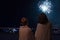 Mother and son looking at New Year celebration fireworks in night sky warmly wrapped in striped plaids standing on home balcony