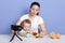 Mother and son playing with toys isolated over blue studio background, making content for her blog, infant being fond of car toy,