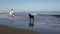 Mother and son walk along the coastline with a huge black dog