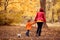 Mother and son walk holding hands in autumn park. Soccer ball laying behind. Mom taking toddler kid back home after football game