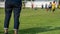 Mother standing and watching her son playing football in a school tournament on a clear sky and sunny day.