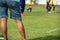 Mother standing and watching her son playing football in a school tournament on a clear sky and sunny day.