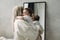A mother stands at the mirror with her one-year-old daughter in her arms, they are reflected in the mirror